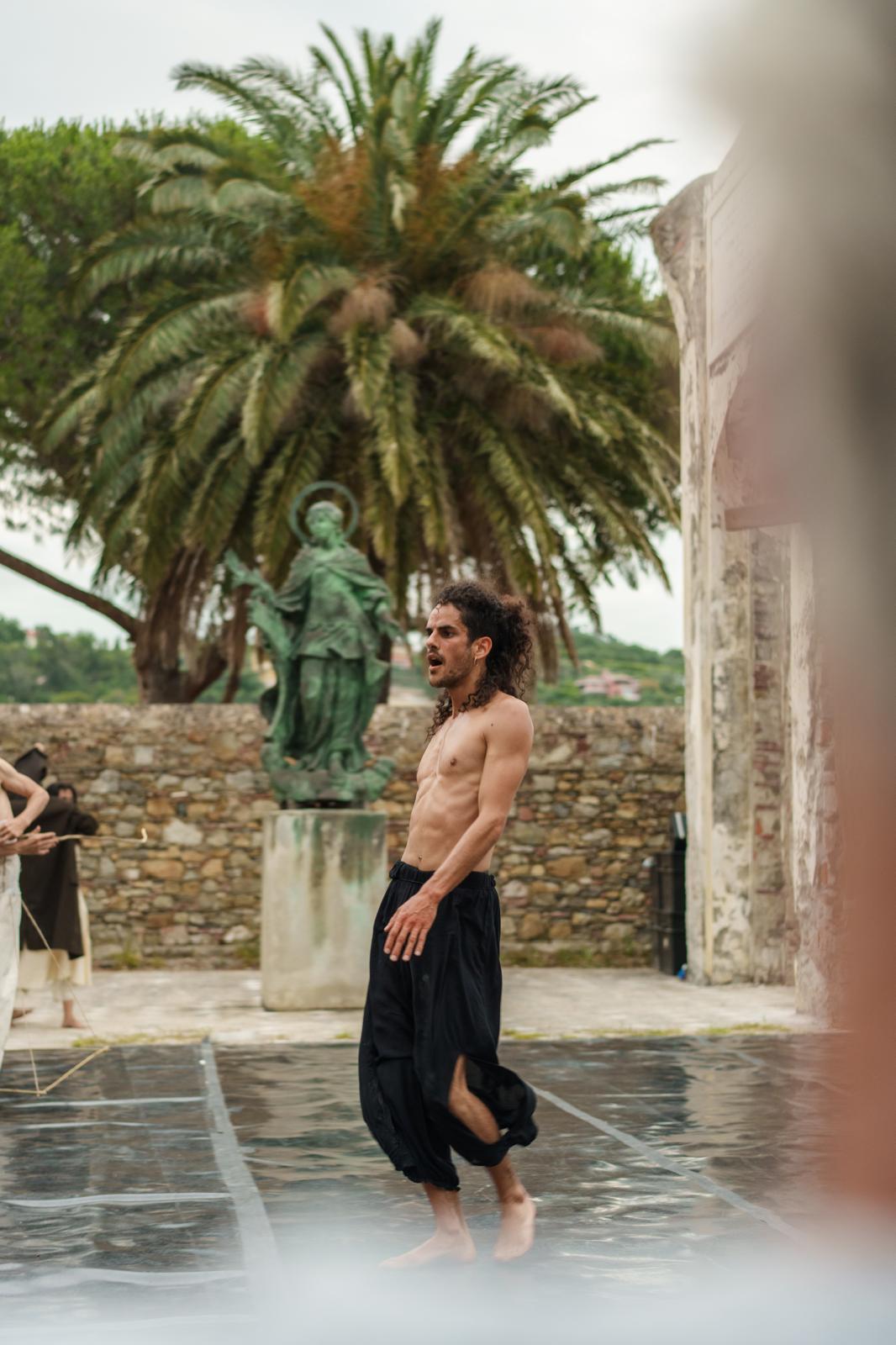 A dancer in black trousers moves alone on an outdoor stage.