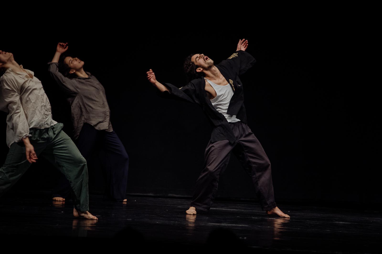 Three dancers move on a dark stage.