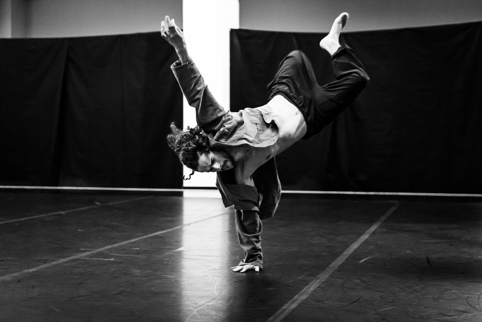 Black-and-white photograph of a dancer in a handstand on a dark stage.