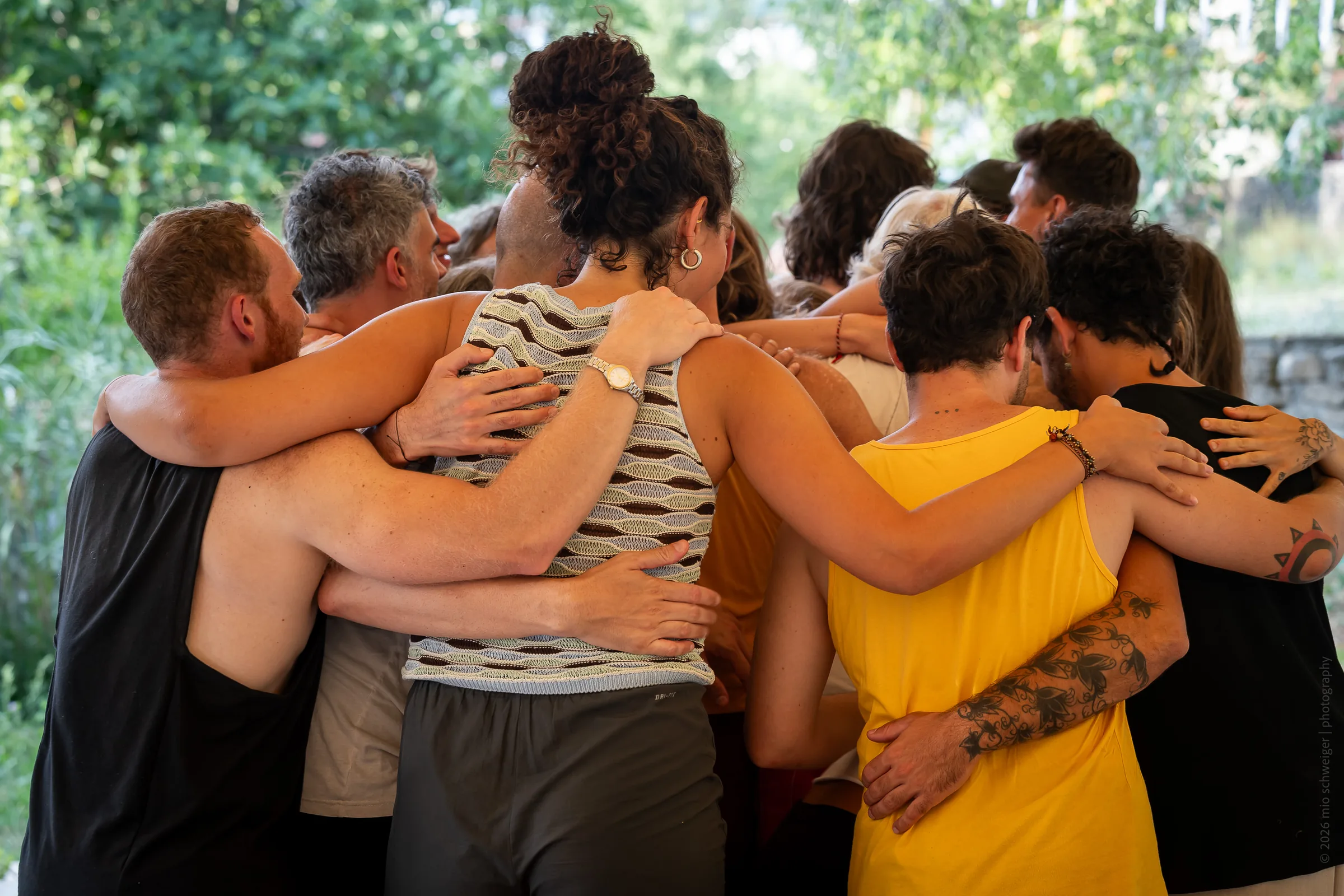 A group stands closely connected with their arms around one another.