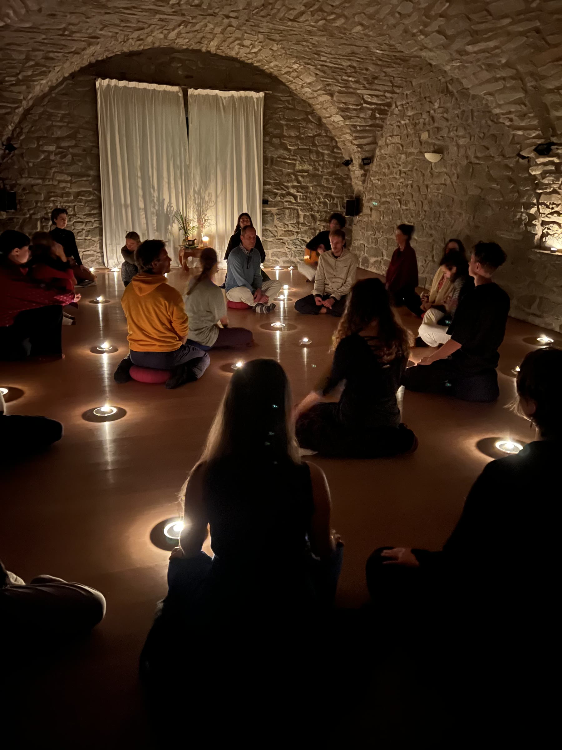 A retreat group sits in a circle of candles in Il Convento’s stone-vaulted room.